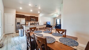 A modern kitchen with dark wooden cabinets, a stainless steel refrigerator, and a microwave. There is a dining area with a wooden table and chairs, and a rug on the floor. - Pet-friendly Lubbock Home - 10 Mi to Downtown (Lubbock)