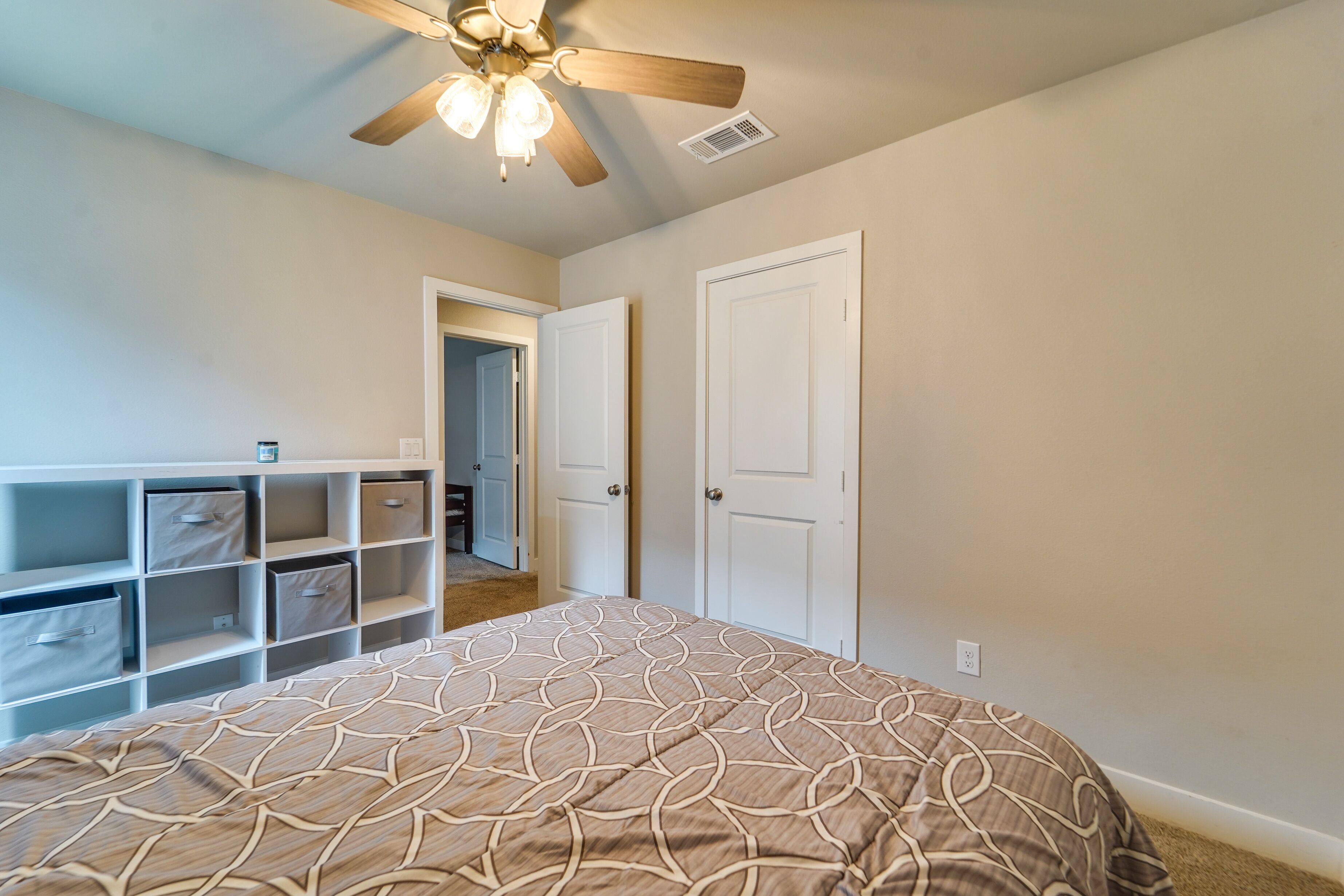 Un dormitorio con cama, almacenamiento integrado, ventilador de techo y una puerta que da a otra habitación.