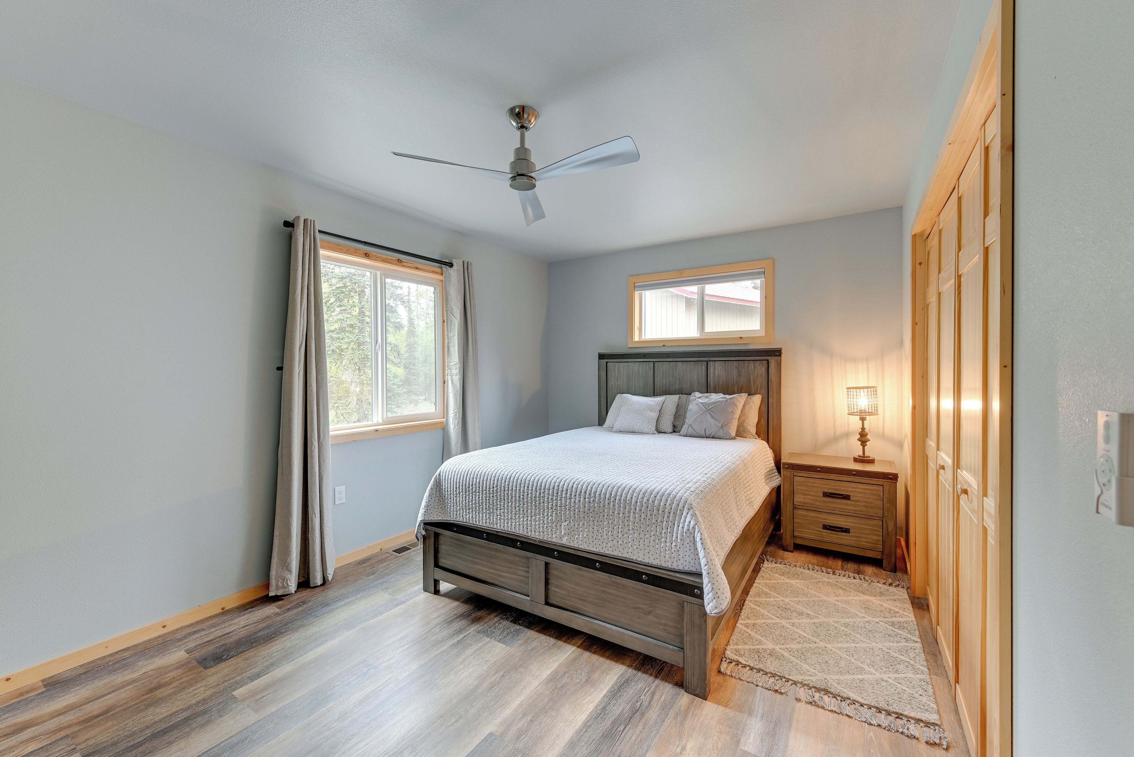 A bedroom with a bed, a nightstand, a ceiling fan, a window, and a door.