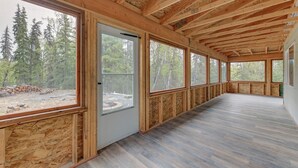 En rummelig stue med store vinduer, træbjælker og udsigt til en skov.