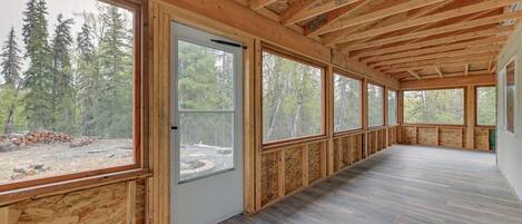 A spacious room with large windows, wooden beams, and a view of a forest.