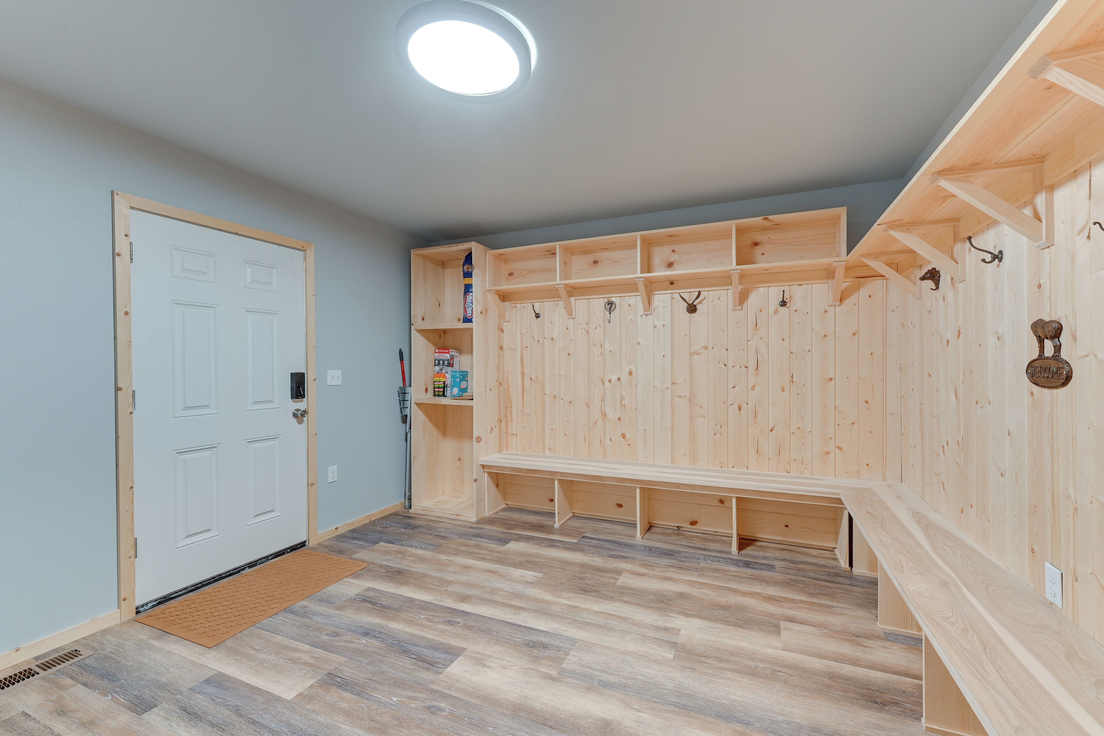 A room with a wooden bench, a door, and a wall-mounted shelf with items.