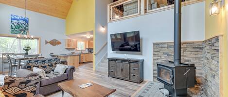 A spacious living area with a high ceiling, a fireplace, a television, and a dining area with wooden furniture.