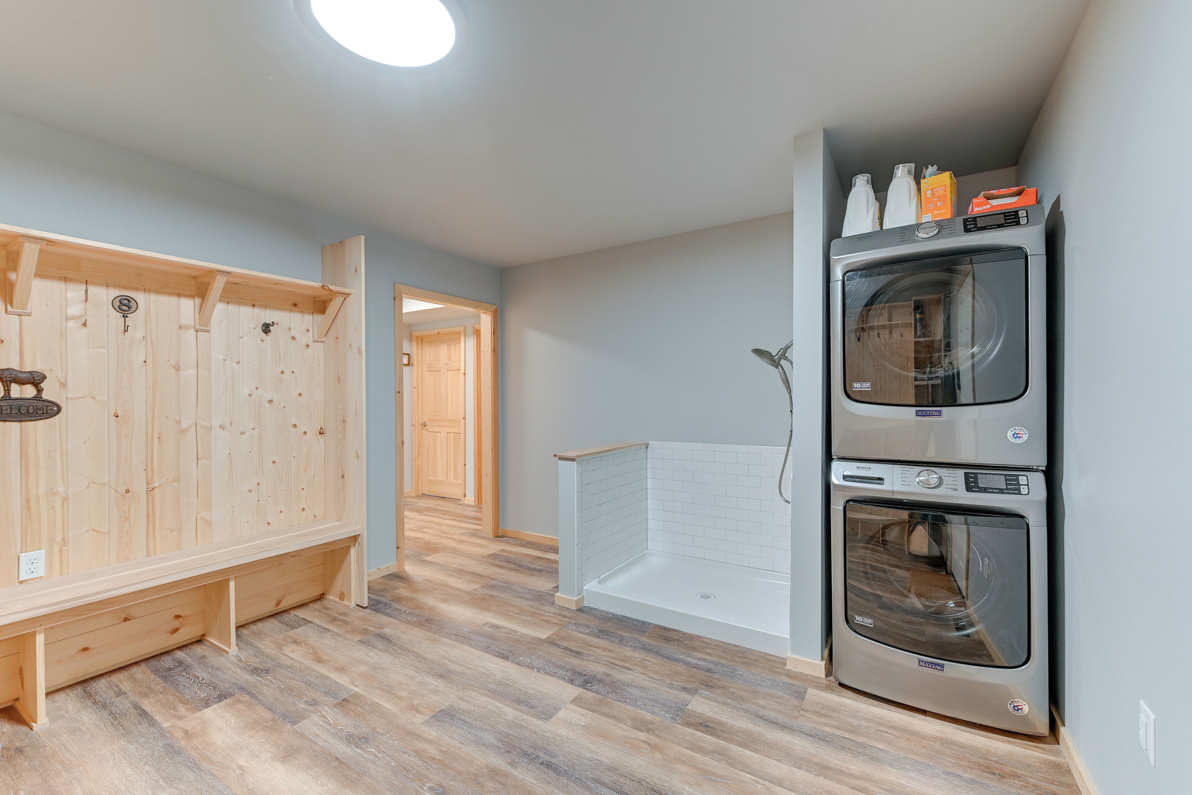 Un lavadero con lavadora y secadora apiladas, bancos de madera y una puerta visible que da a otra habitación.
