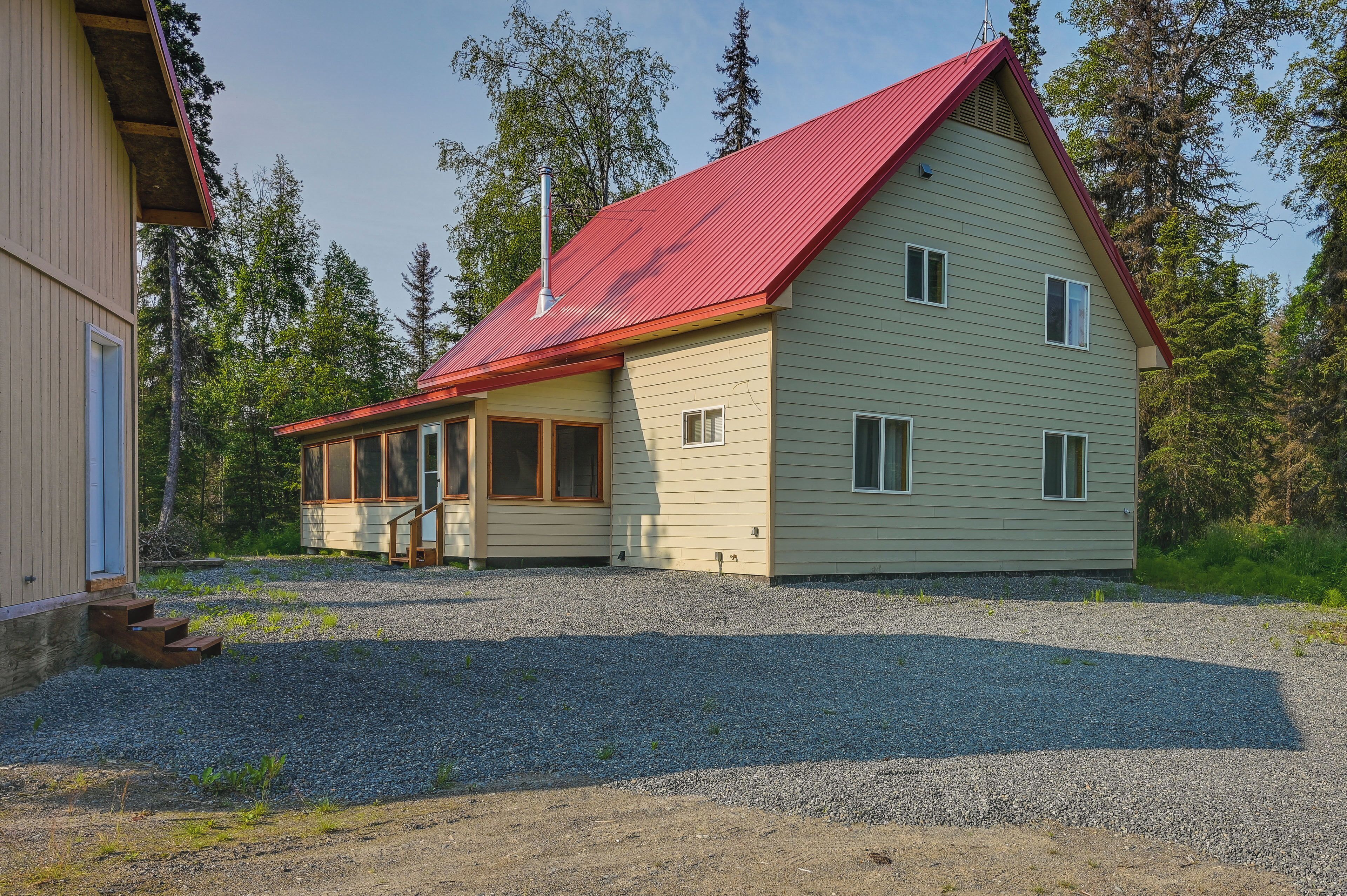 A two-story house with a red roof, a front porch, and a gravel driveway.