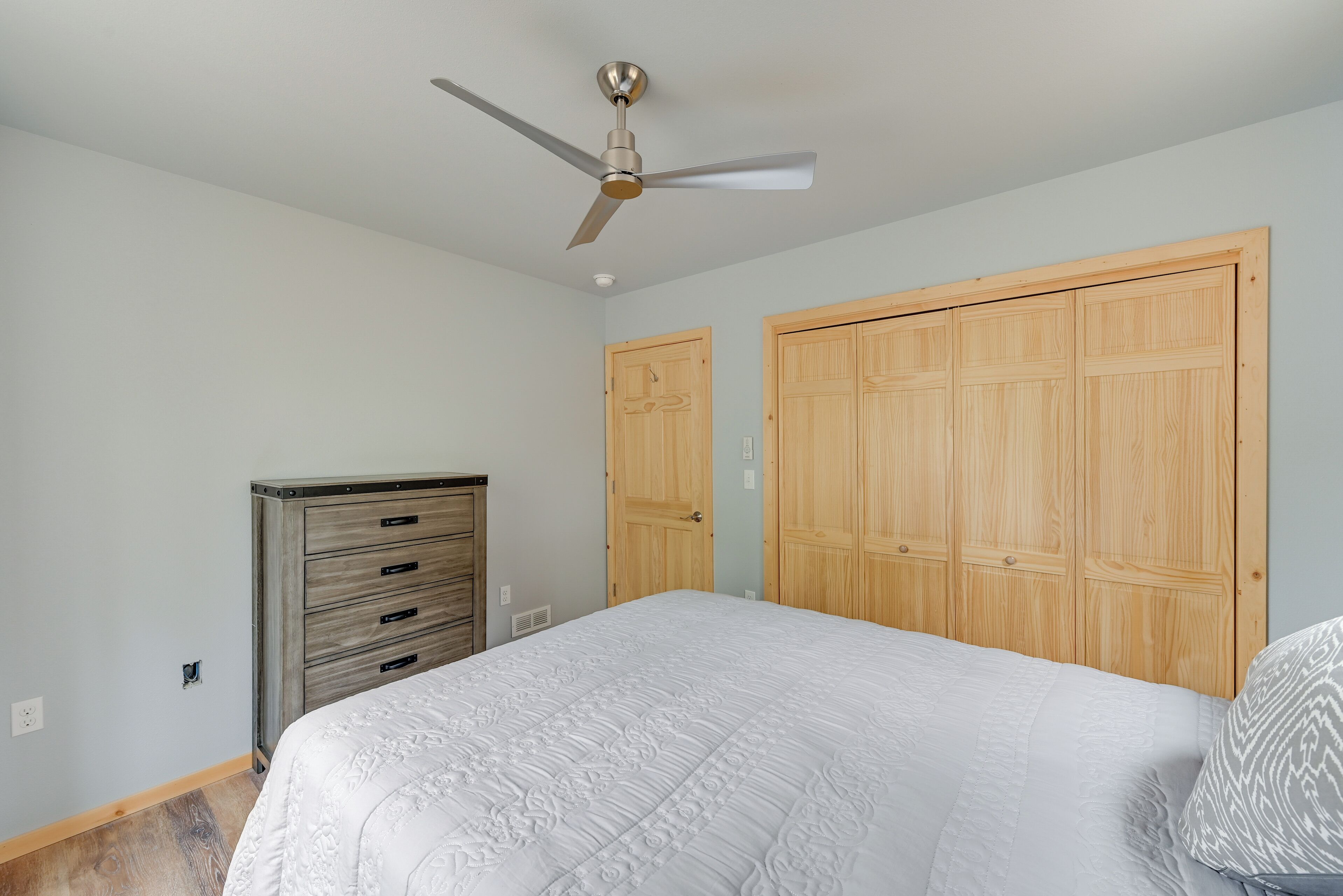 Ein Schlafzimmer mit einem Bett, einem Deckenventilator, Holzschränken und einer Kommode.