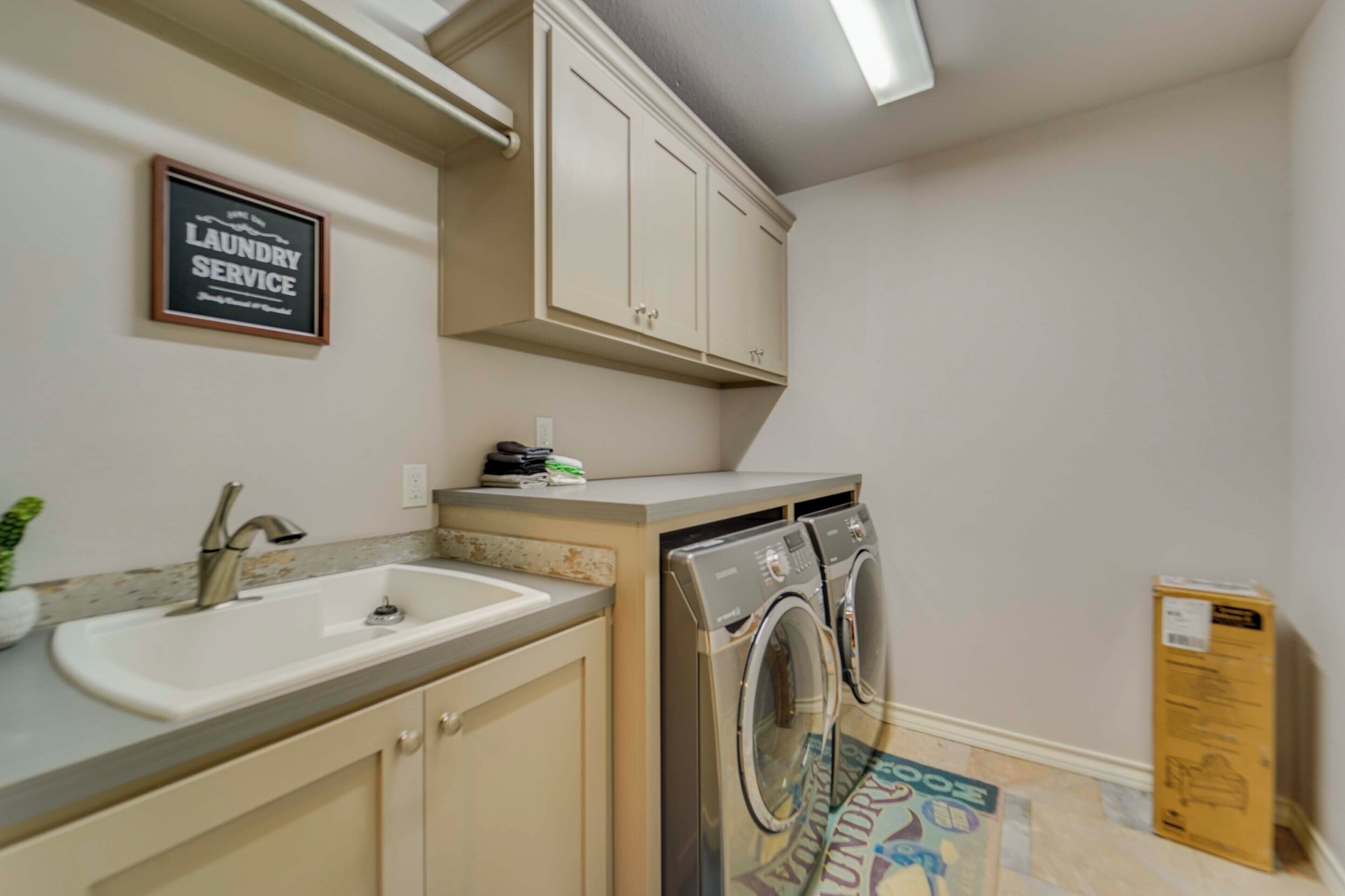 A laundry service sign, a sink, a countertop, and a washing machine in a room.