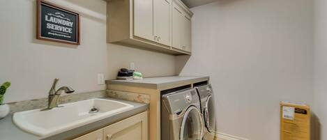 A laundry service sign, a sink, a countertop, and a washing machine in a room.