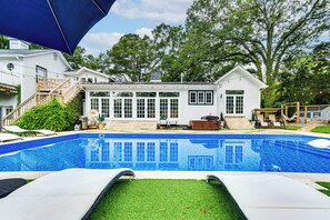 A backyard with a swimming pool, a covered patio, and a house with a large windowed porch. - Spacious Durham Home w/ Fire Pit & Hot Tub! (Durham)