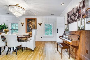 A dining area with a wooden table, white chairs, a chandelier, and a piano. - Spacious Durham Home w/ Fire Pit & Hot Tub! (Durham)