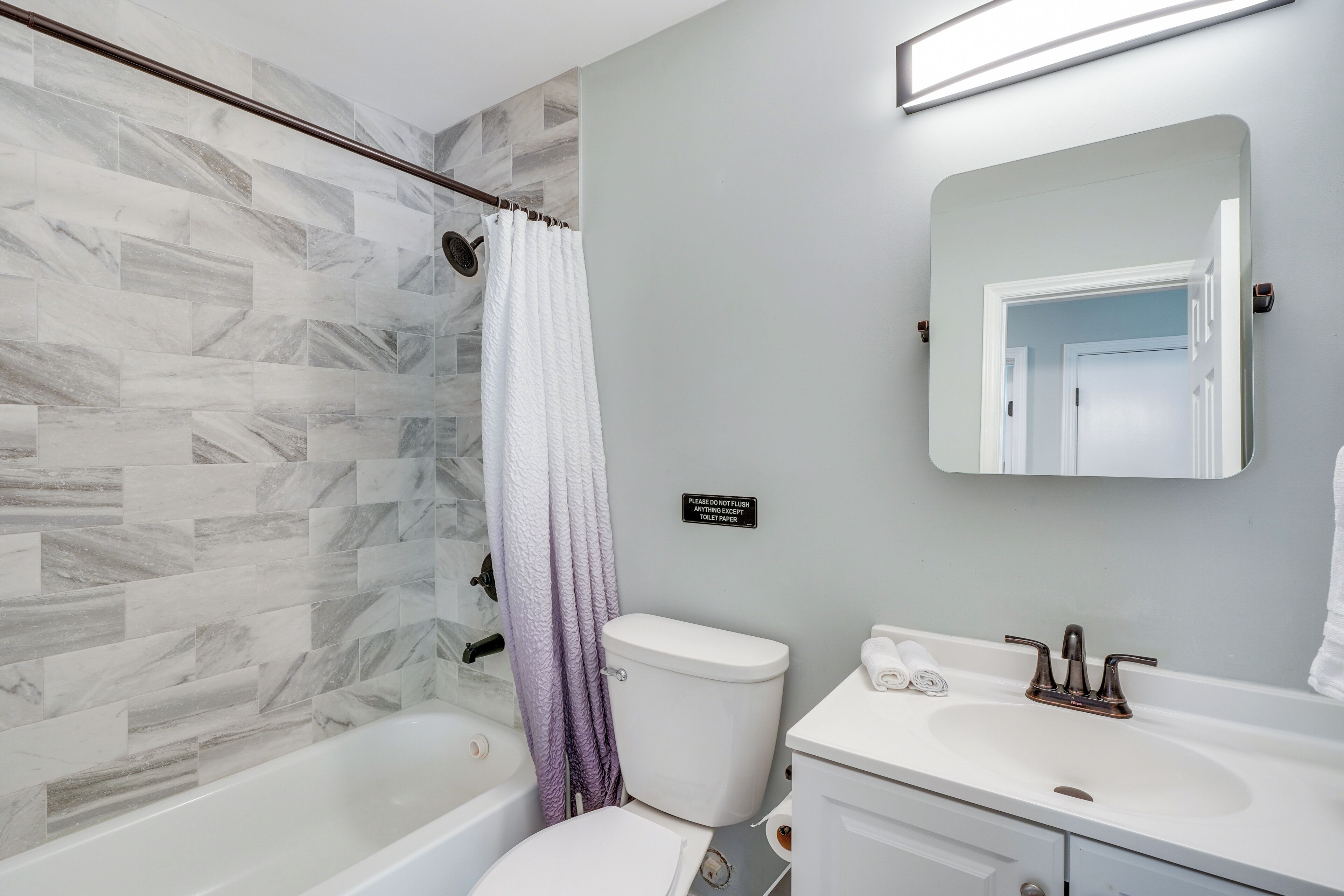 A bathroom with a marble tile wall, a bathtub, a toilet, a sink, and a mirror.