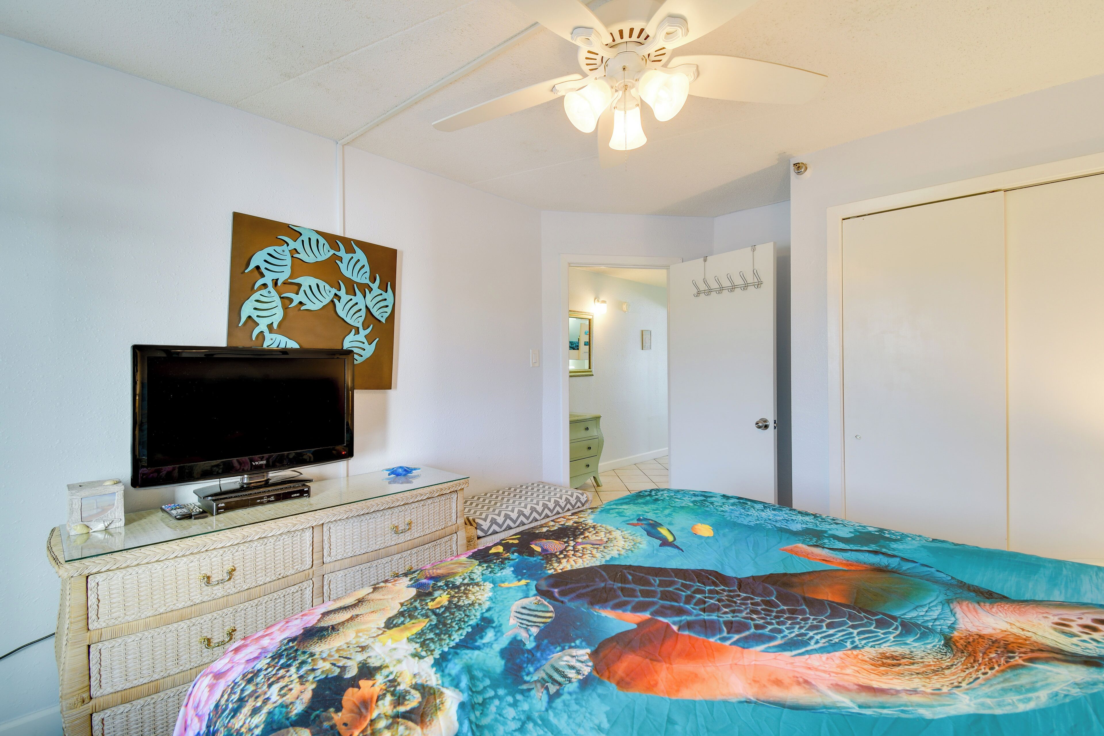 Un dormitorio con cama, televisión, cómoda y ventilador de techo.