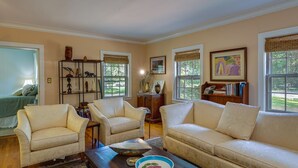 A living room with a beige sofa, two armchairs, a coffee table, and a bookshelf. - Spacious Durham Apartment Near Downtown (Durham)