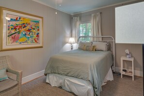 A bedroom with a bed, a chair, a bedside table, a lamp, a window with curtains, and a framed painting on the wall. - Spacious Durham Apartment Near Downtown (Durham)