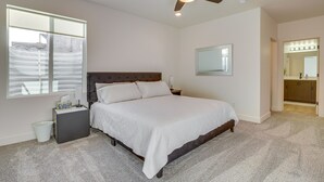 Ein Schlafzimmer mit einem großen Bett, einem Deckenventilator, einem Nachttisch, einem Schminktisch, einem Spiegel und einem Fenster mit Jalousien.