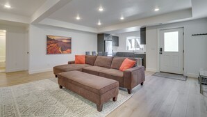 Ein geräumiges Wohnzimmer mit einem Ecksofa, einem passenden Hocker und einem großen Teppich.