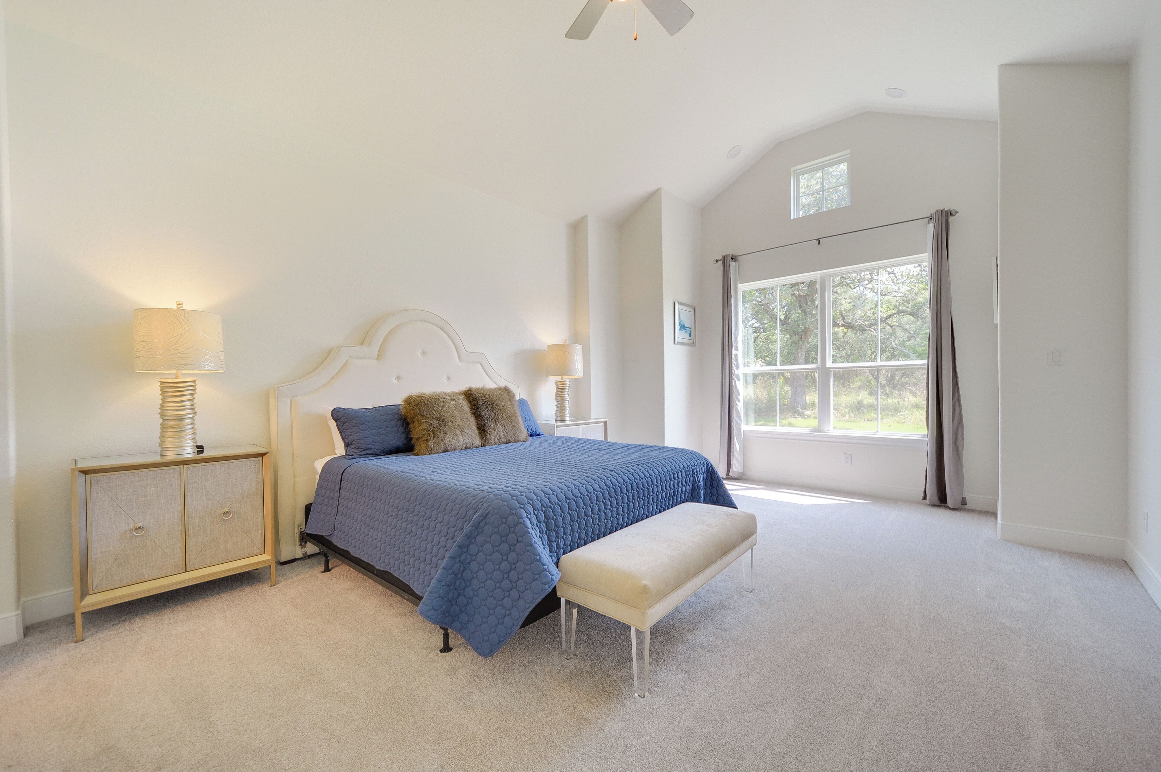 A bedroom with a large bed, two bedside tables, a bench, and a window with curtains.