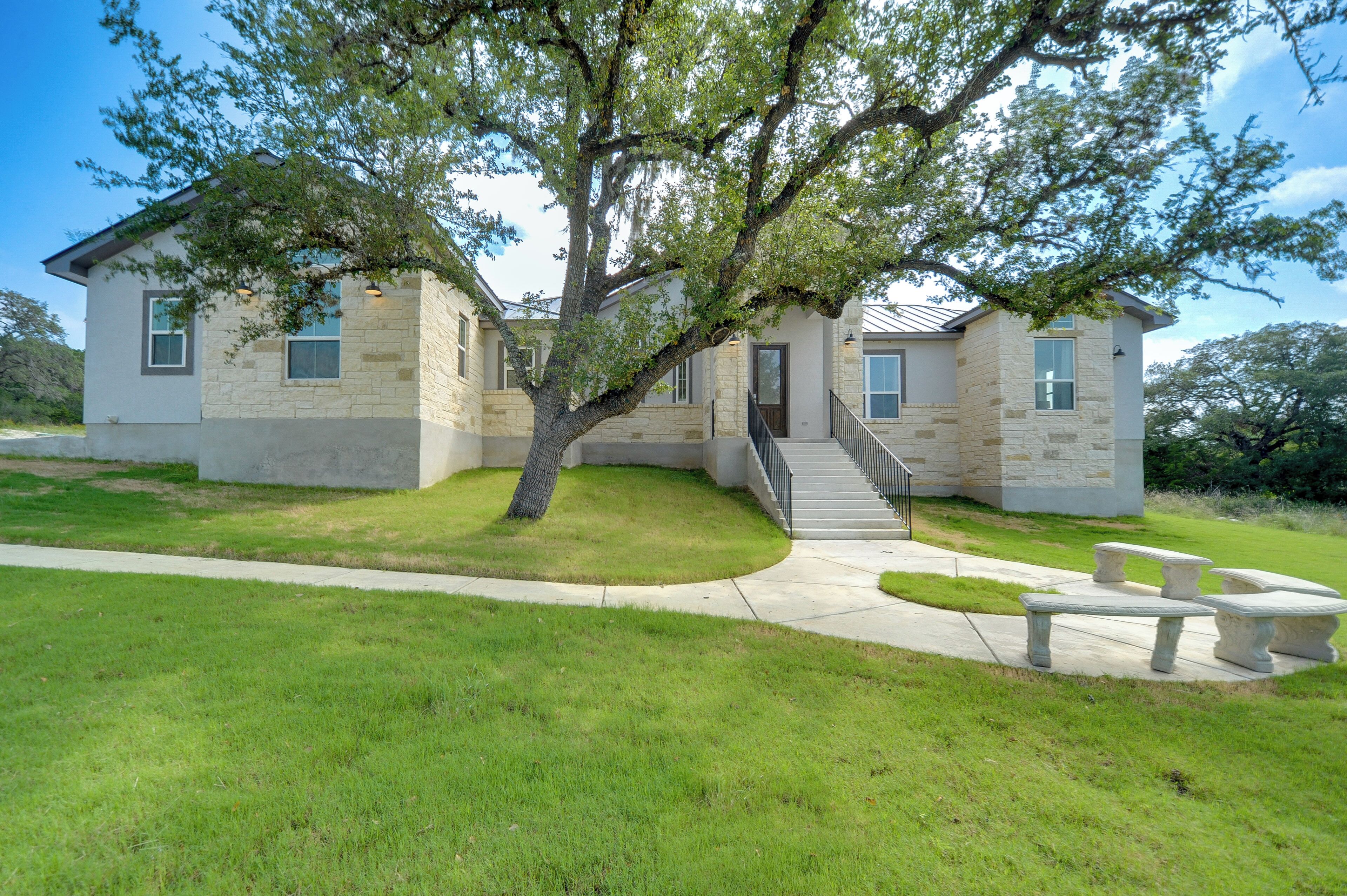 A two-story house with a stone facade, a large tree in front, and a paved driveway.