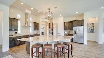 A spacious kitchen with a large island, dark wooden cabinets, and a stainless steel refrigerator.