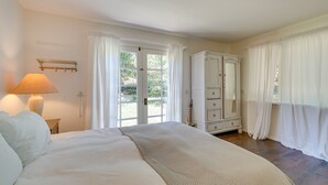 A bedroom with a bed, a dresser, a lamp, and a window with curtains. - Farmhouse-chic Carpinteria Cottage w/ Pool Access (Carpinteria)