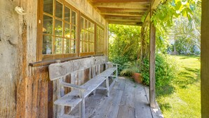 A wooden porch with a bench and a large window overlooking a garden. - Farmhouse-chic Carpinteria Cottage w/ Pool Access (Carpinteria)