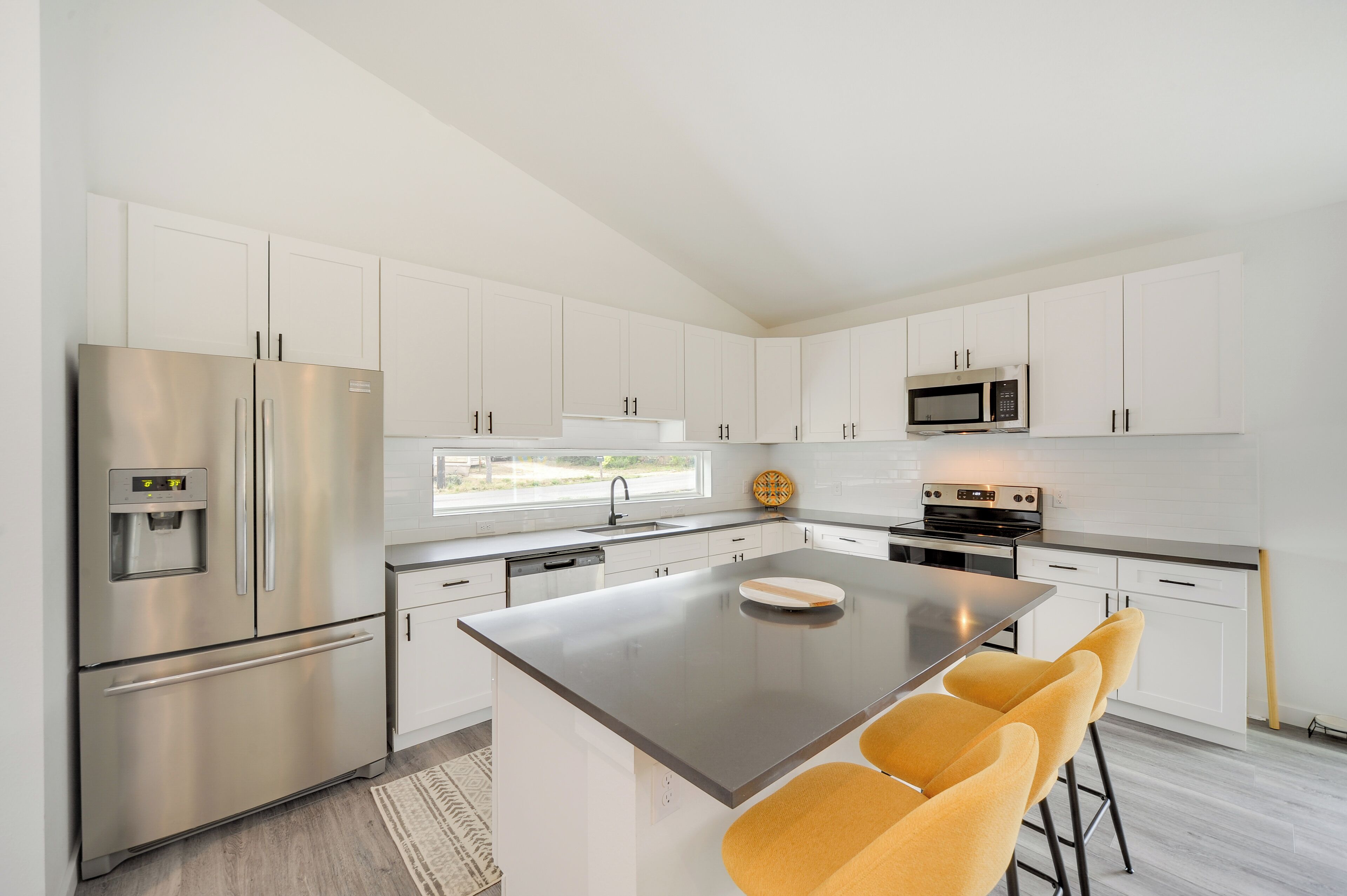 A modern kitchen with white cabinets, stainless steel appliances, and a central island with yellow bar stools.