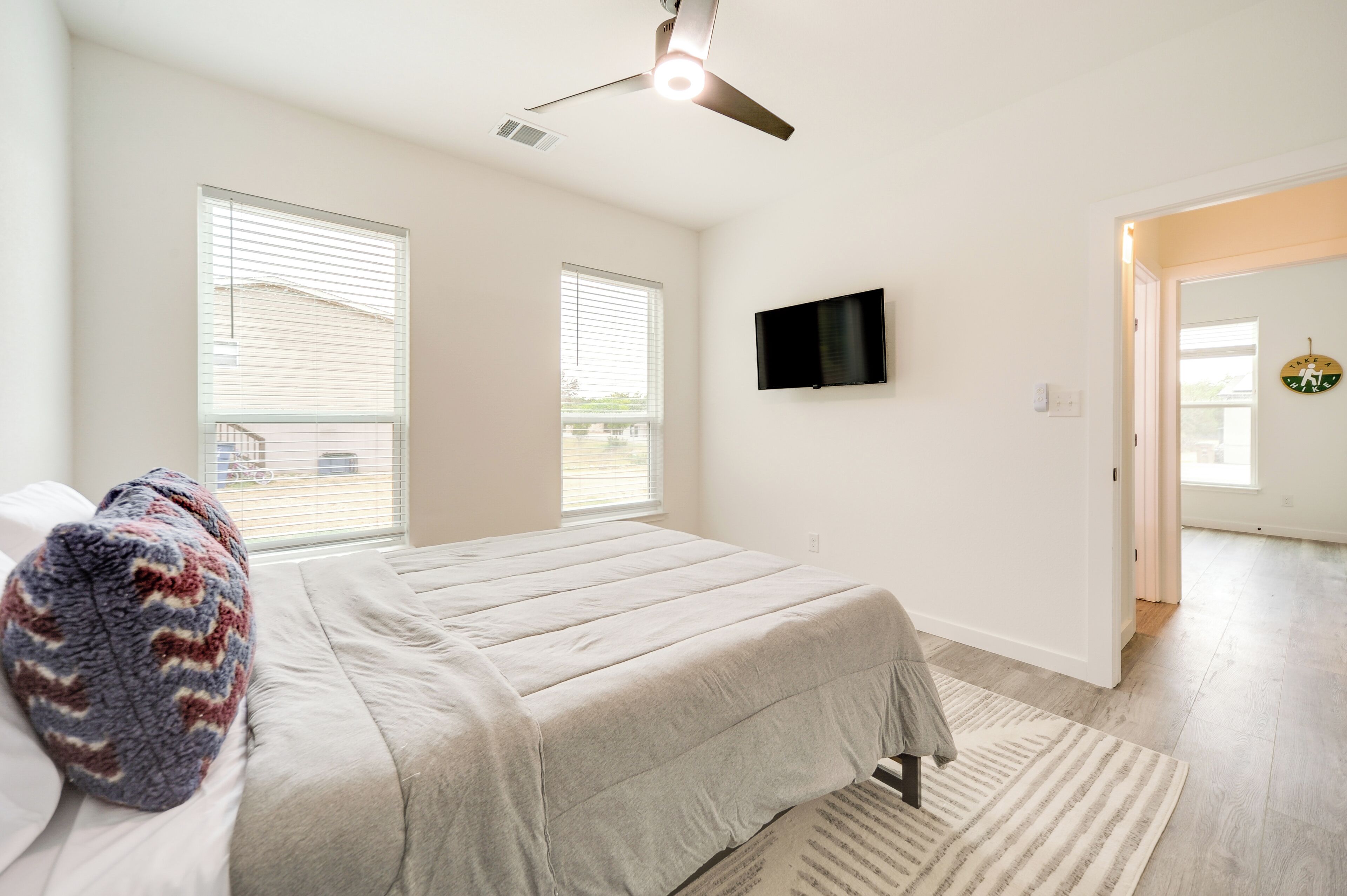 Un dormitorio con cama, ventilador de techo, televisor y ventana.
