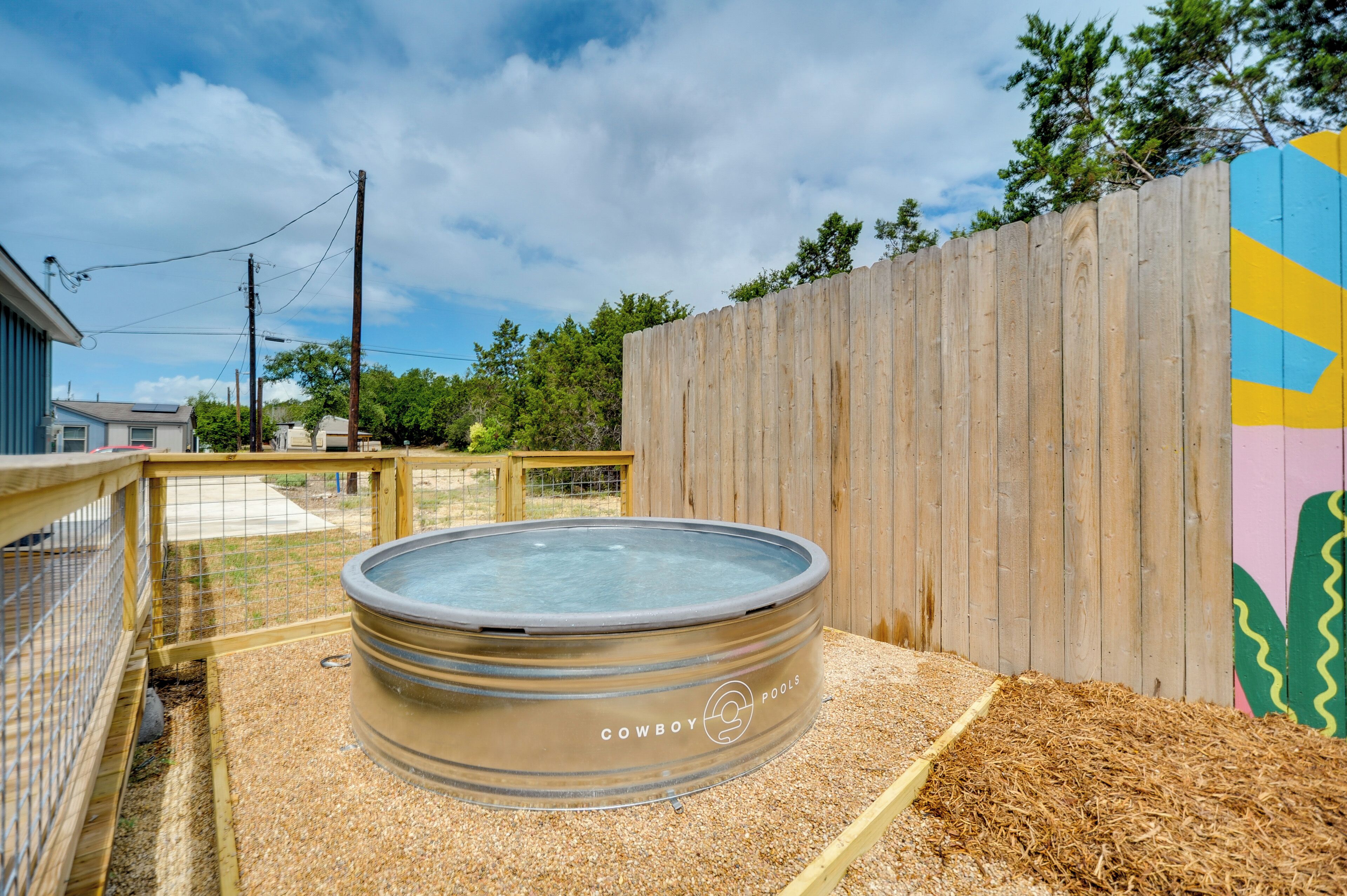 Un jacuzzi con la etiqueta "Cowboy Pools" en un área exterior cercada, con valla de madera y césped.