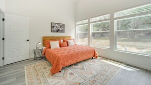 Un dormitorio con una cama grande, un cabecero de madera, una mesita de noche con lámpara, una alfombra y una ventana con vistas a árboles.