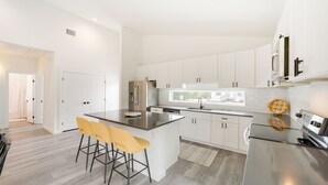 Una cocina moderna con armarios blancos, una isla de acero inoxidable y un ventanal grande.