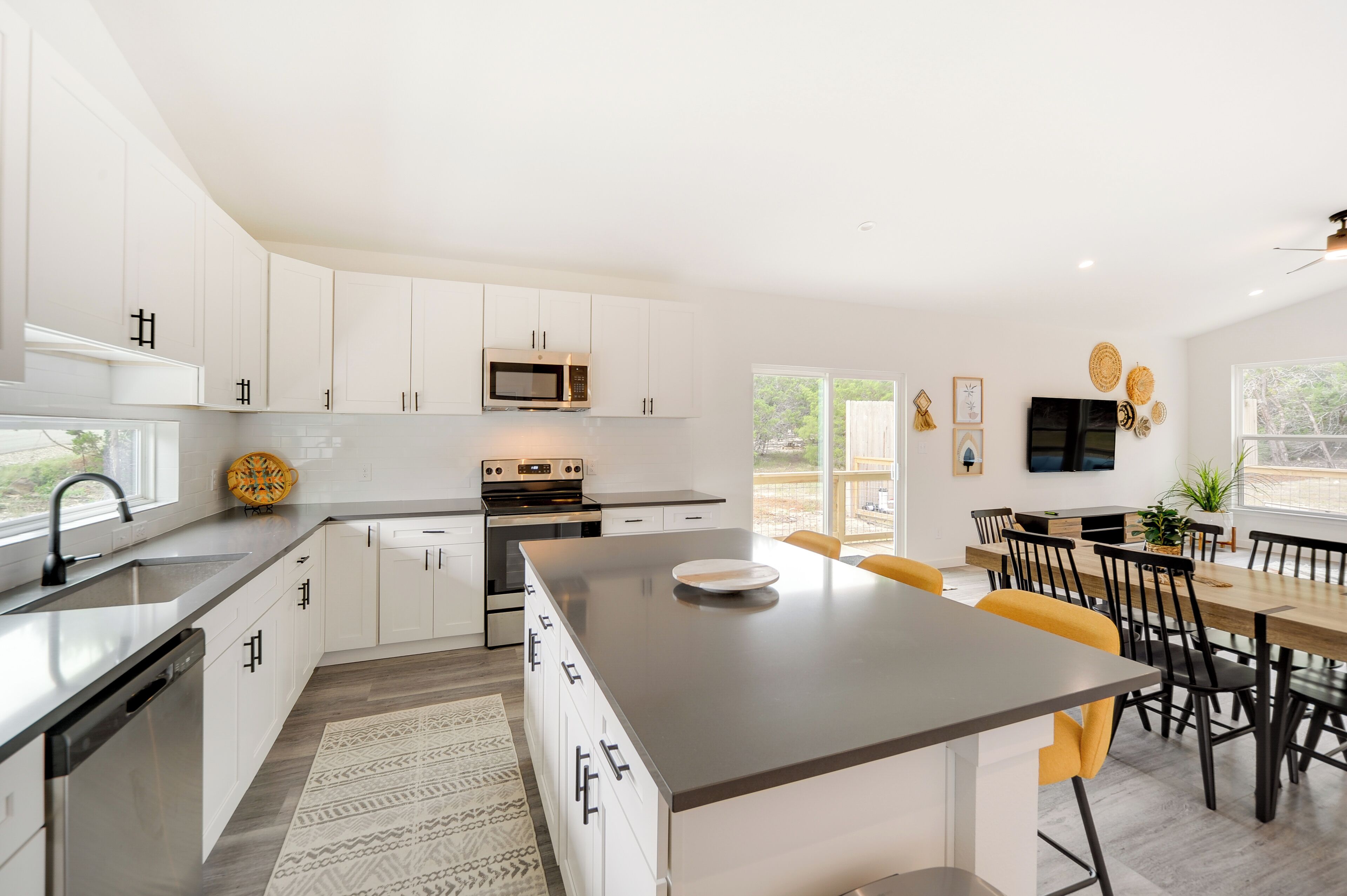 A modern kitchen with white cabinets, a central island, and a dining area with a wooden table and chairs.
