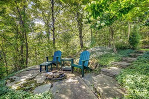 A forested area with a seating arrangement of two Adirondack chairs and a small table, surrounded by rocks and greenery. - Warren Vacation Rental ~ 3 Mi to Sugarbush Resort! (Warren)