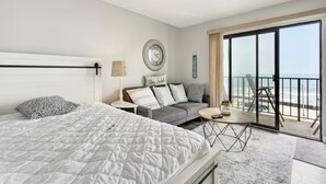 A hotel room with a large bed, a sofa, a small table, and a balcony with a view of the beach. - Beachfront Fourth-floor Condo w/ Community Pool! (North Wildwood)