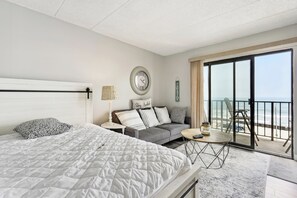 A hotel room with a large bed, a sofa, a small table, and a balcony with a view of the beach. - Beachfront Fourth-floor Condo w/ Community Pool! (North Wildwood)