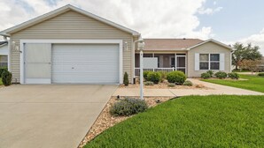 Une maison de plain-pied avec une porte de garage blanche, un porche à l’avant et une pelouse bien entretenue.