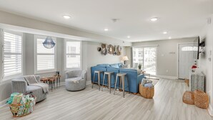 Un salón amplio con un sofá azul, sillones grises y una mesa de centro. Hay cestos de mimbre y una lámpara en el suelo.