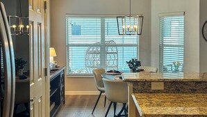 A kitchen with a granite countertop, a Bosch dishwasher, and a dining area with a white chair and a table. - Private Lanai & Pool Access: Home in the Villages! (The Villages)