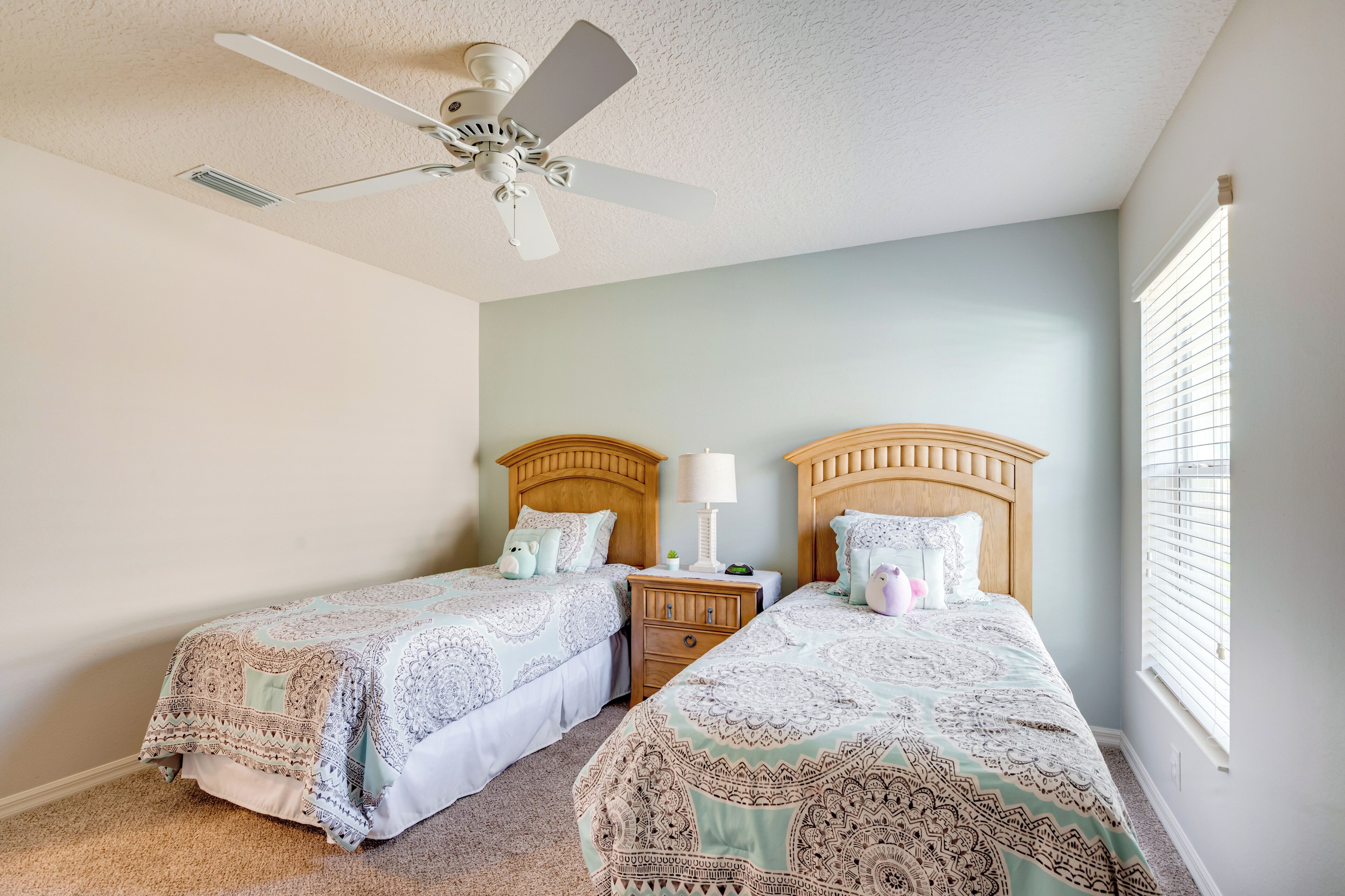 A bedroom with two beds, a ceiling fan, and a window with blinds.