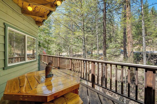 A wooden deck with a bench and a bird sculpture, overlooking a forested area.