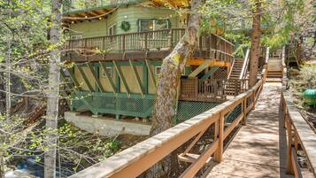 Escape to a secluded cabin surrounded by trees and a serene stream, accessible via a wooden bridge.