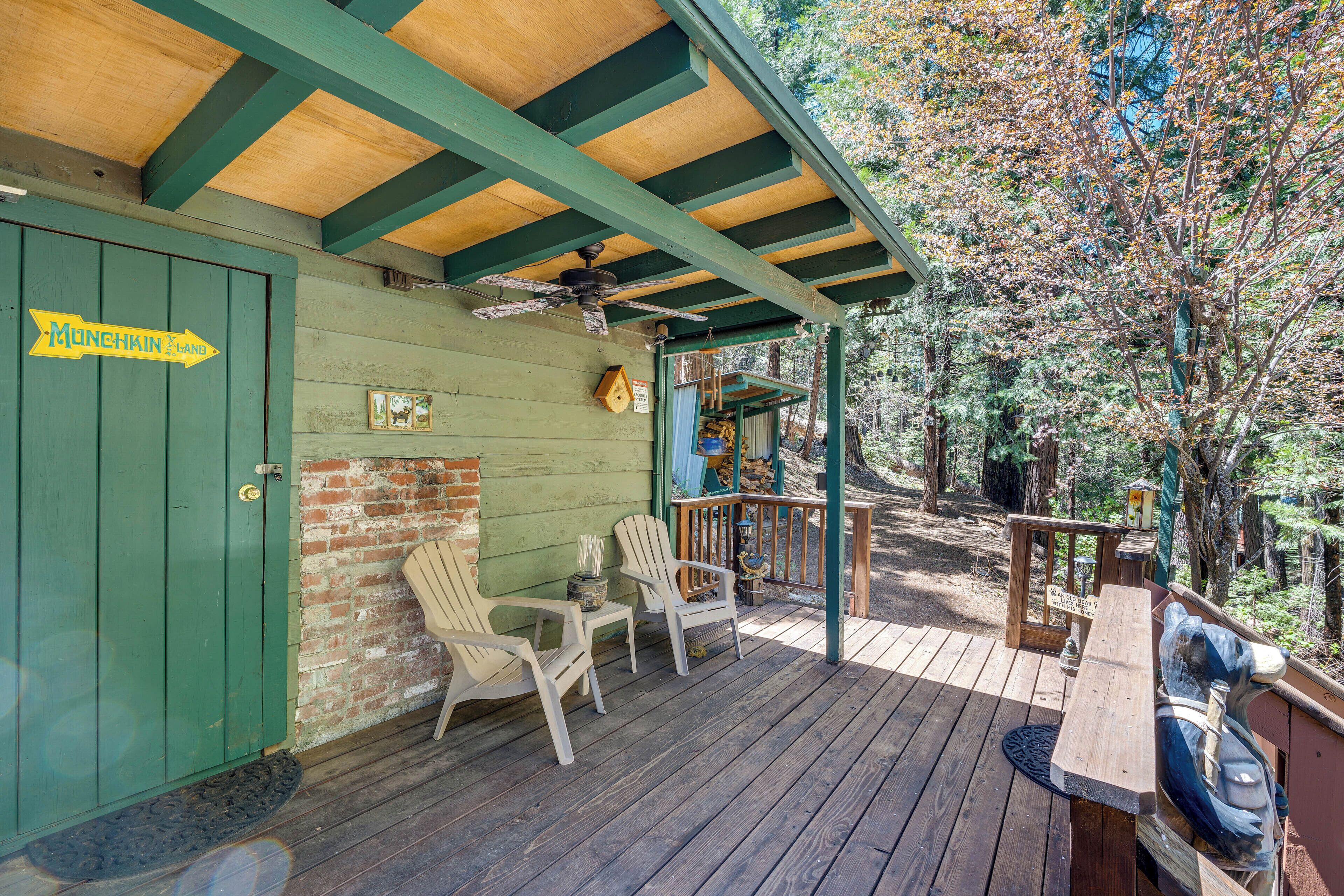 A wooden deck with Adirondack chairs and a picnic table, a green door with a sign, and a view of trees.