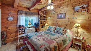 Une chambre confortable dans un chalet, avec un plafond en bois, un lit recouvert d’une courtepointe, une table de chevet, une commode et une fenêtre avec des rideaux.