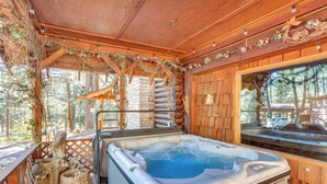 Un bain à remous dans un chalet en bois, avec une terrasse en bois, un escalier en bois et une vue sur la forêt environnante.