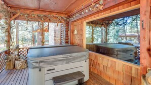 Une cabane en bois dotée d’un bain à remous, d’une terrasse en bois et offrant une vue sur la forêt environnante.