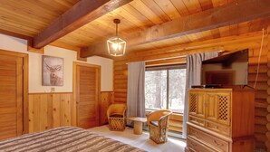 Une chambre située dans un chalet en rondins, comprenant un lit, deux chaises, une commode et un téléviseur.