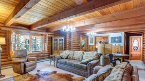 L’intérieur d’une cabane en rondins, avec un plafond en bois, des canapés en cuir, un tapis en fourrure et un coin repas.