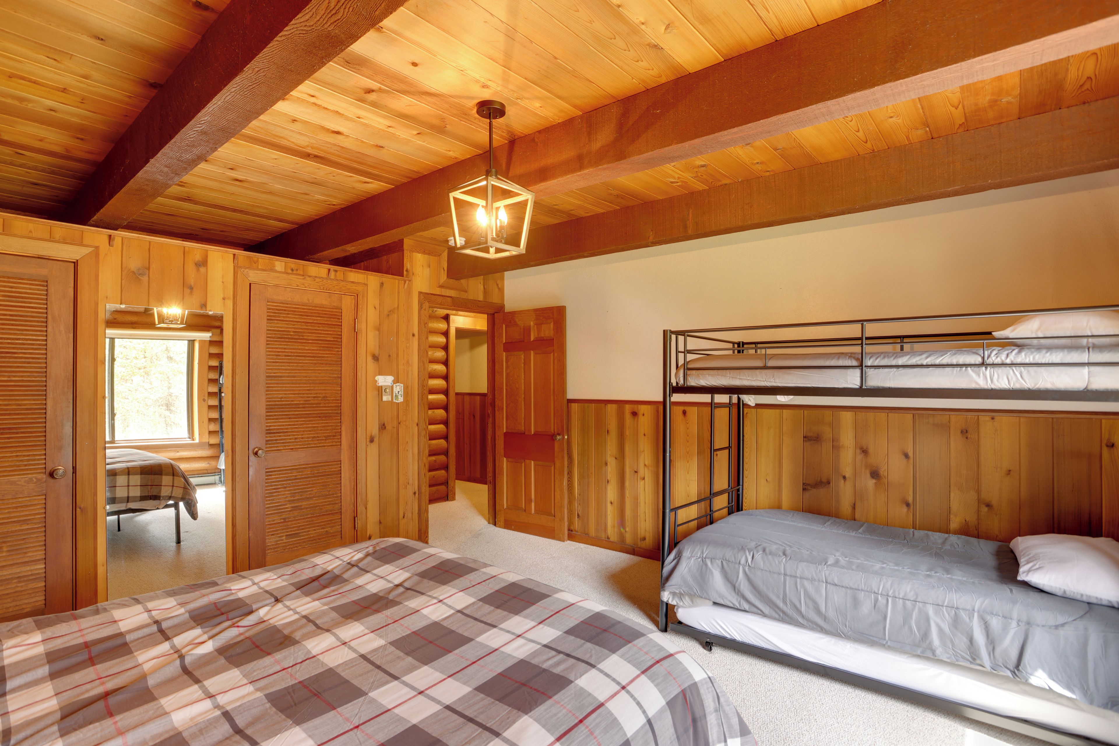 A wooden cabin bedroom with a bunk bed, a plaid bedspread, and a hanging light fixture.