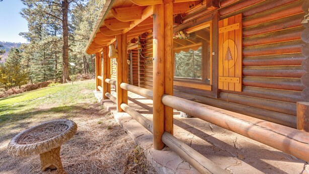 Une cabane en rondins dotée d’un porche couvert, de balustrades en bois et d  ’un abreuvoir à oiseaux en pierre.