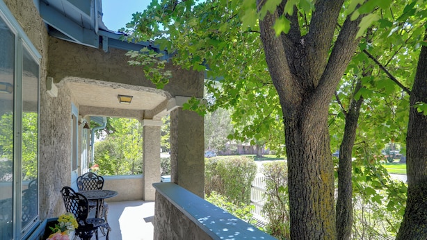Un balcon avec une table et des chaises, une fenêtre ornée de fleurs et une vue sur des arbres et une clôture.
