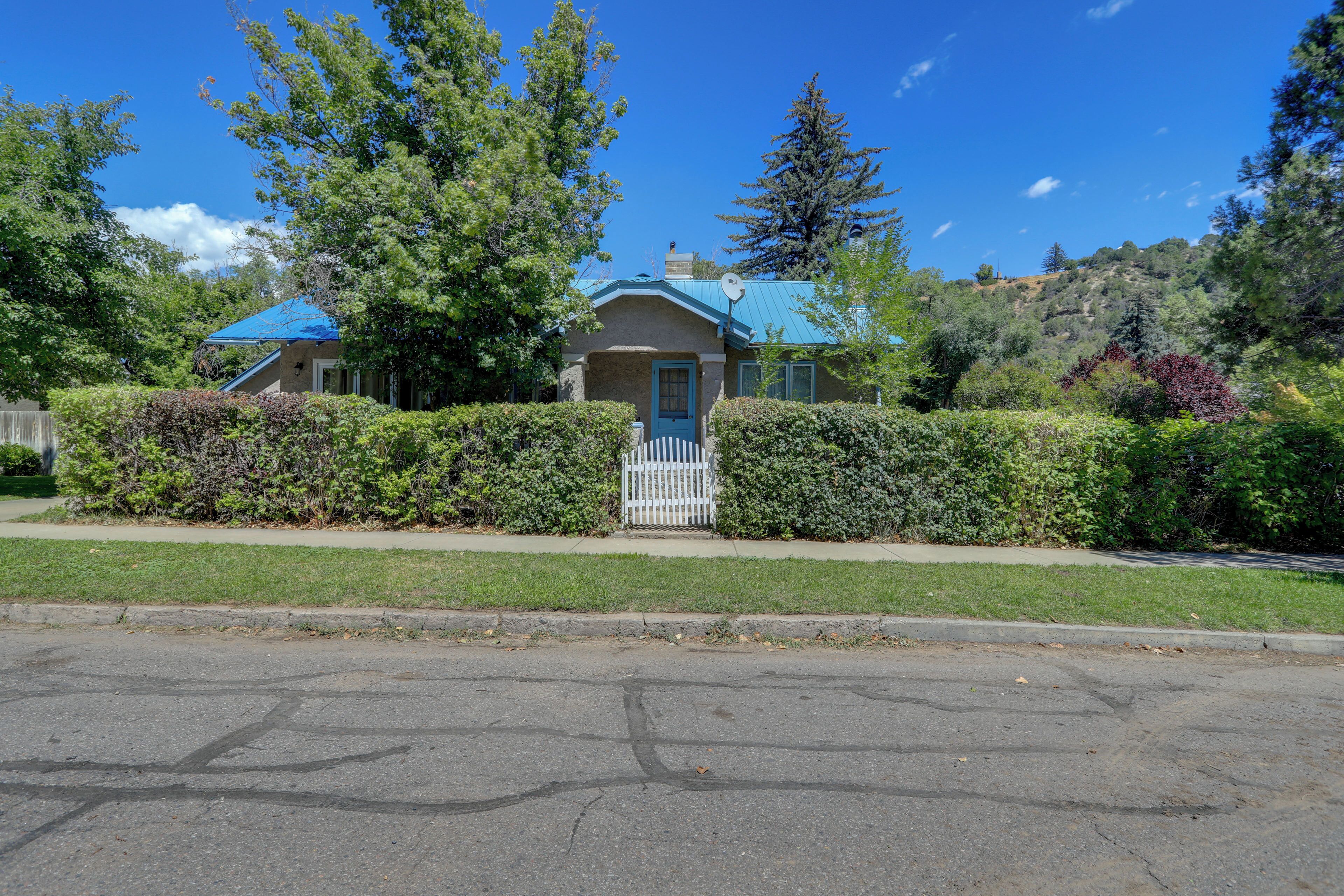 A house with a blue roof, surrounded by greenery and a clear sky.